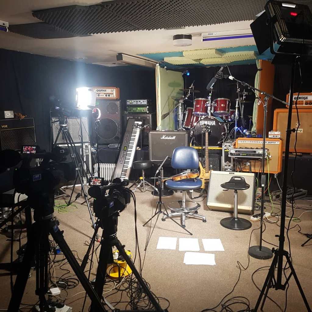 a mulit-camera set up in music studio. A chair in the middle is lit. On it is a violin.