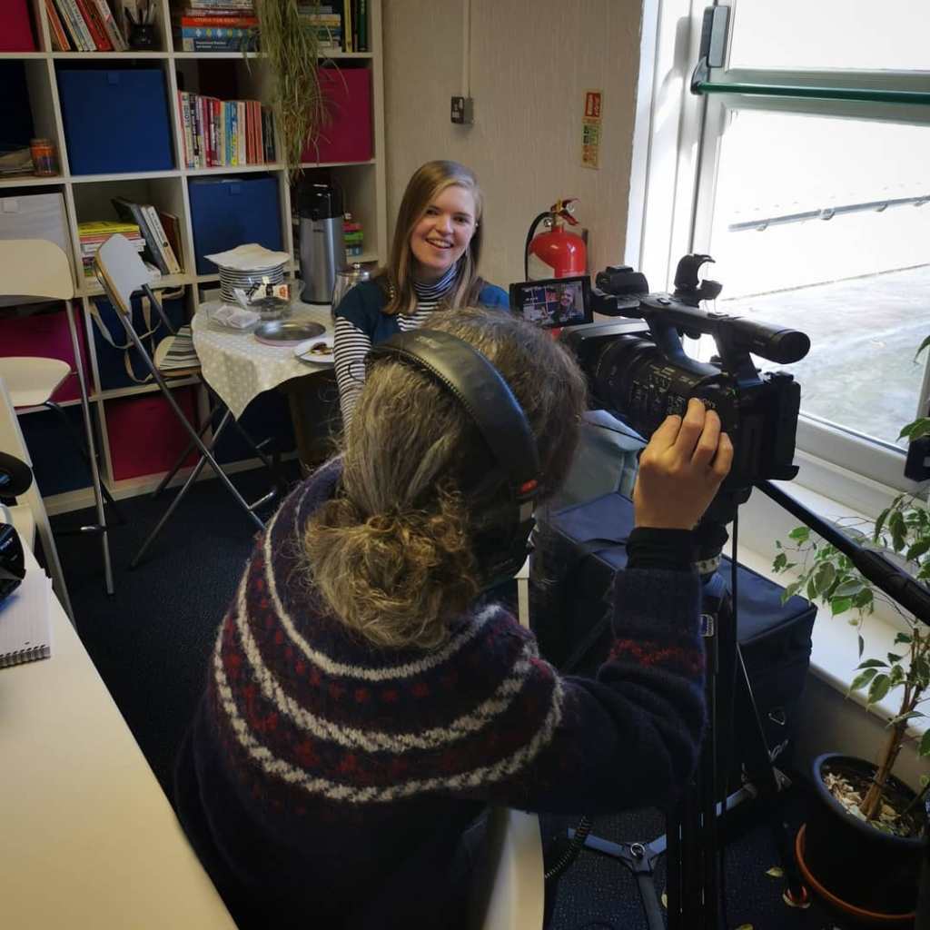 A person adjusts the settings on a video camera as they prepare to film someone else. 